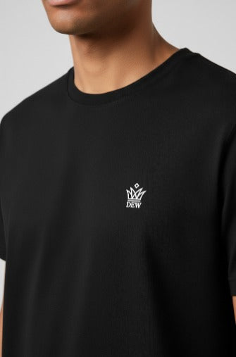 Man wearing DEW 100% Cotton black t-shirt with a small embroidered Dew white logo on a gray background