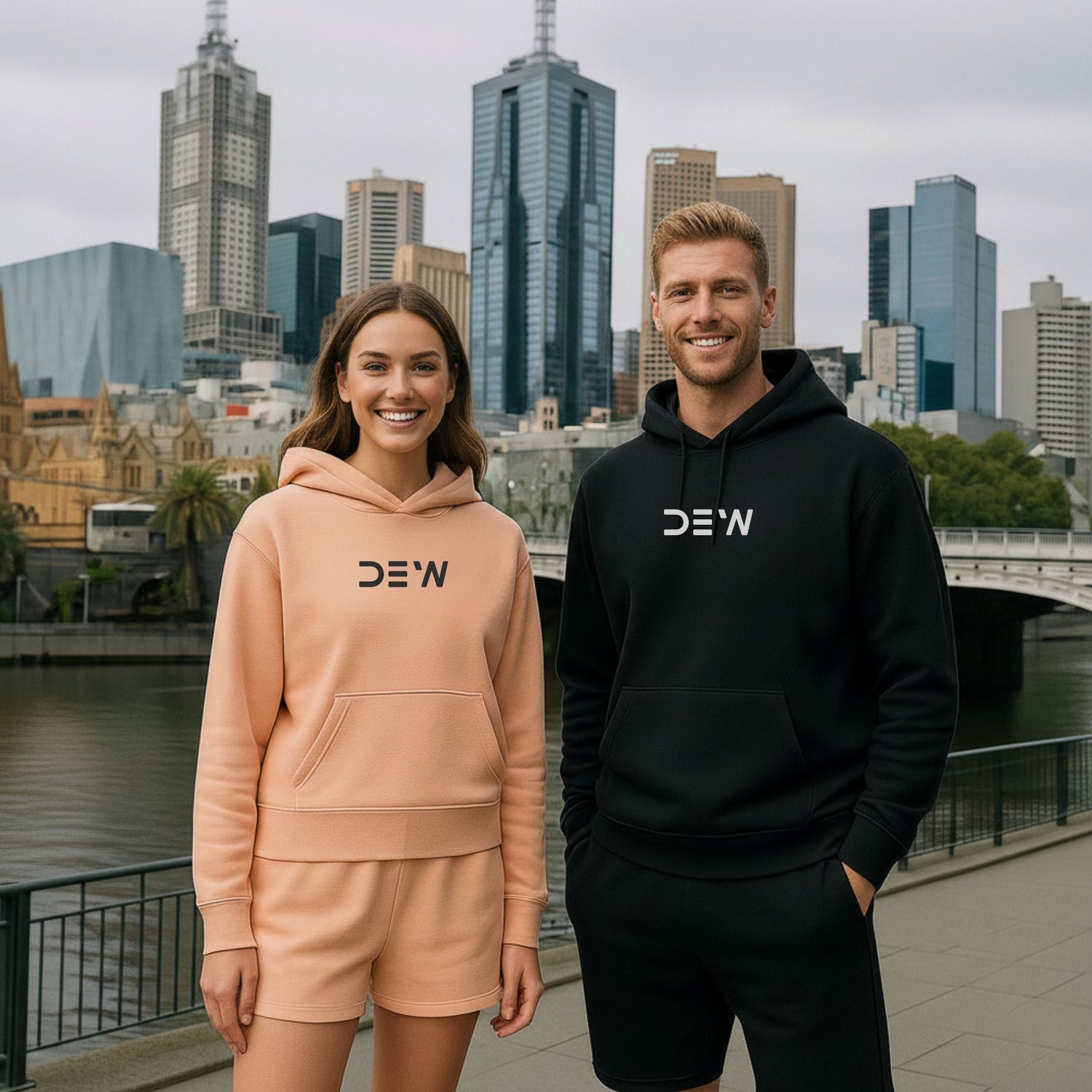Woman and man wearing DEW Unisex Hoodies and Activewear Shorts in front of the Melbourne skyline. Image highlights Australian streetwear and comfort.