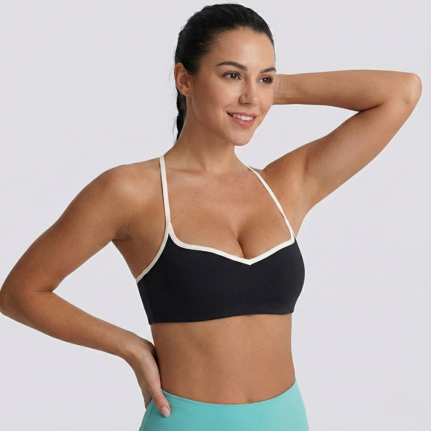 Woman wearing a black DEW Elevate Bra with white straps on a plain background