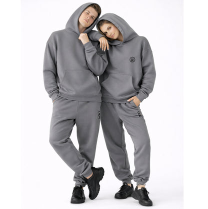 Two people wearing matching gray hoodie and pants sets on a white background