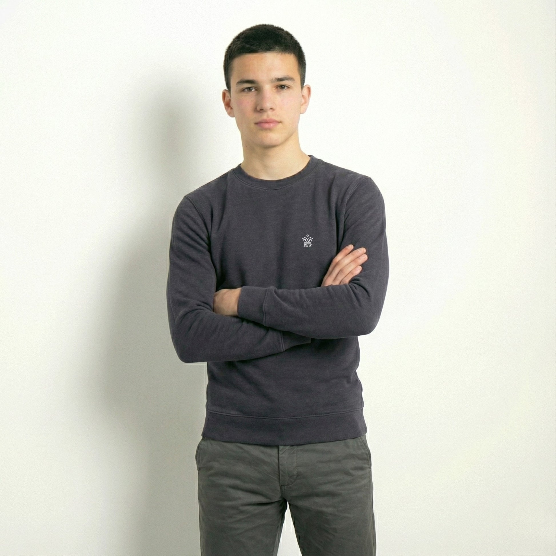 Person wearing a dark gray sweater with a small logo on a plain background