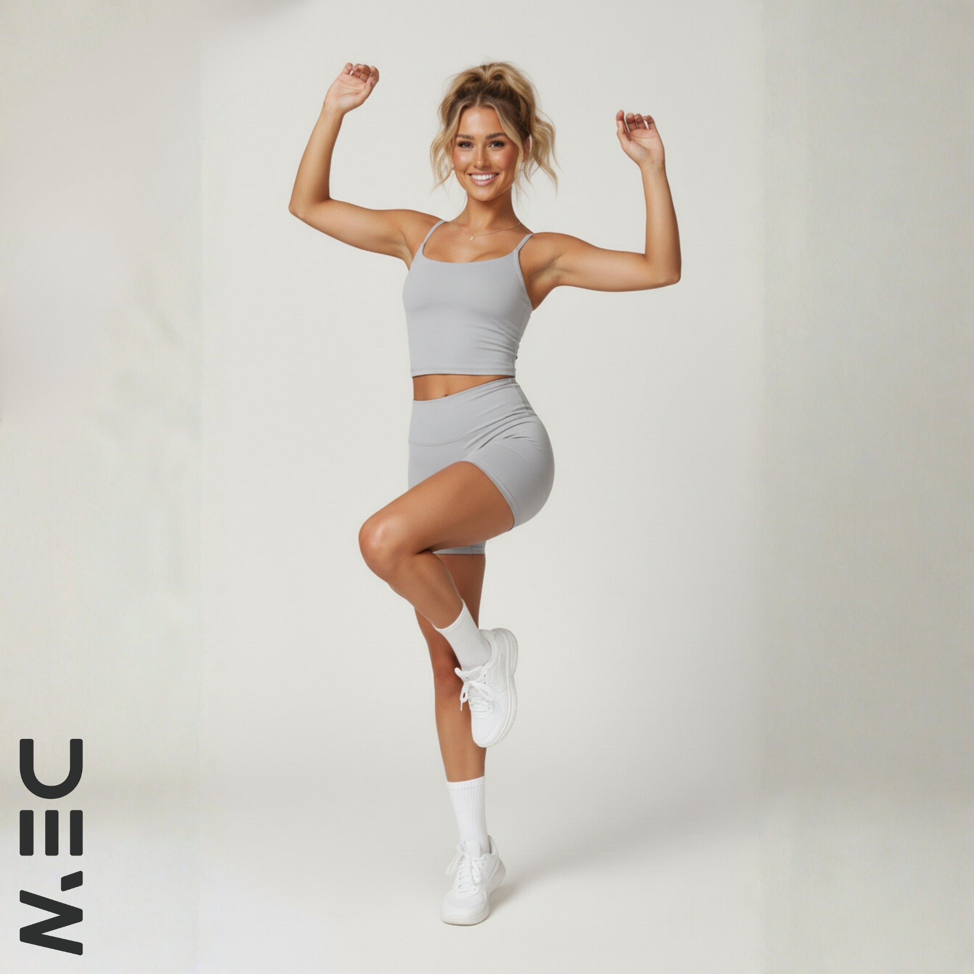 Woman in gray dew luxe cami top posing with arms raised on a white background, featuring the brand 'NIN'.