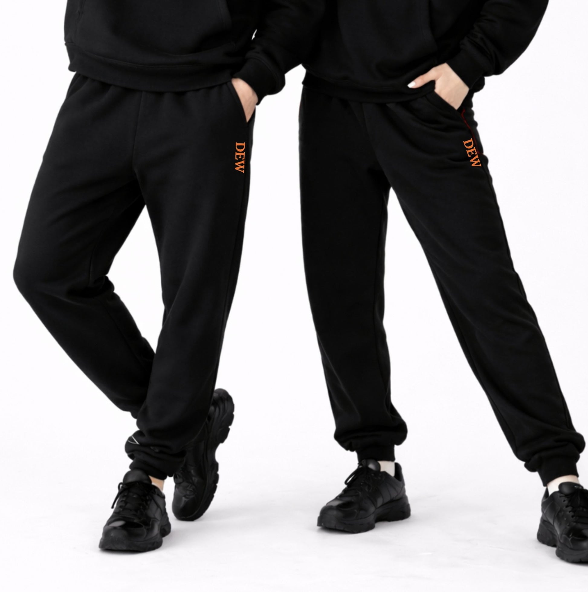 Two people wearing black tracksuits with 'DEW' branding on a white background