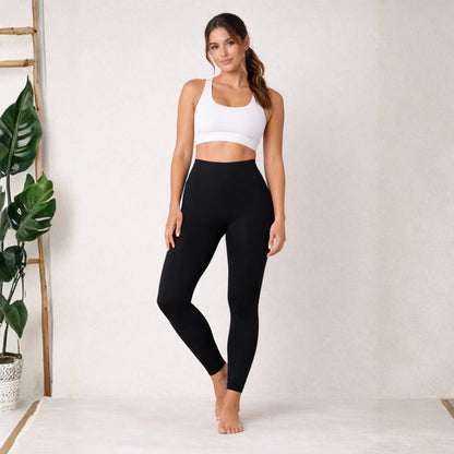 Woman wearing a white sports bra and dew black leggings standing against a white background.