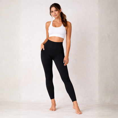 Woman wearing Dew  black leggings and a white sports bra on a plain background