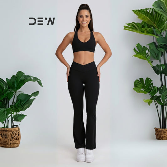Woman in black athletic wear-flow fit flares standing between two potted plants with 'DEW' branding. 