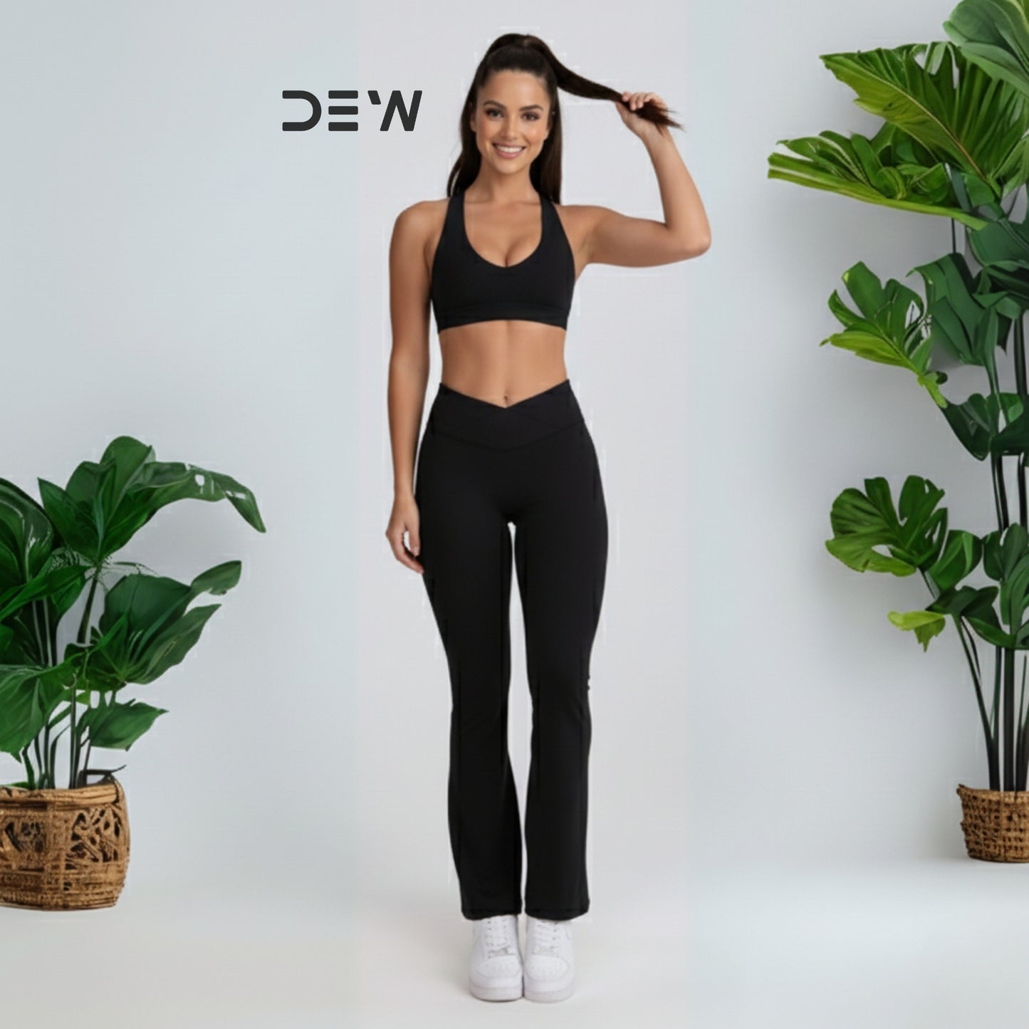 Woman wearing black seamless sports bra and Flow Fit Flare leggings. Studio shot with plants, highlighting DEW branding.