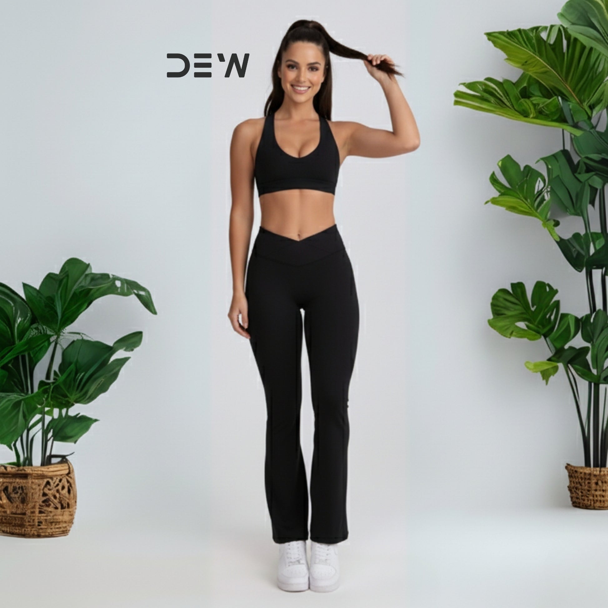 Woman wearing black seamless sports bra and Flow Fit Flare leggings. Studio shot with plants, highlighting DEW branding.