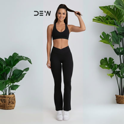 Woman wearing black seamless sports bra and Flow Fit Flare leggings. Studio shot with plants, highlighting DEW branding.