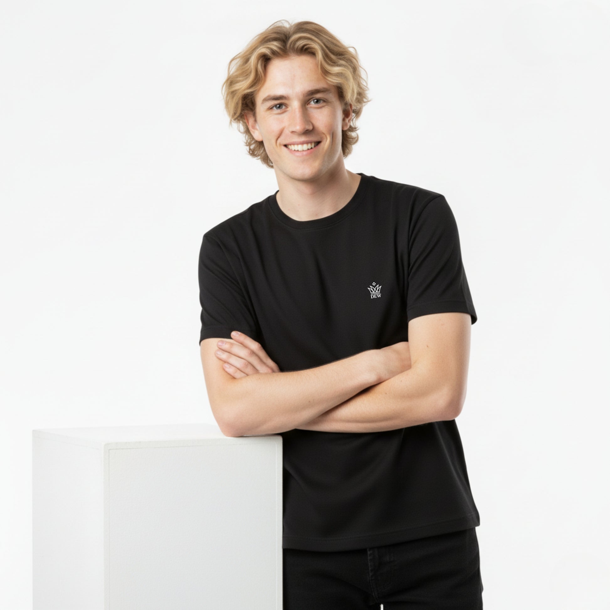 Person wearing a DEW 100% Cotton black t-shirt  with a small DEW embroidered logo, standing against a white background
