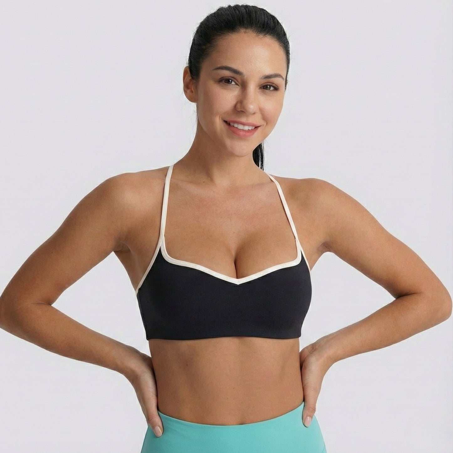 Woman wearing a black DEW Elevate sports bra with white straps on a plain background