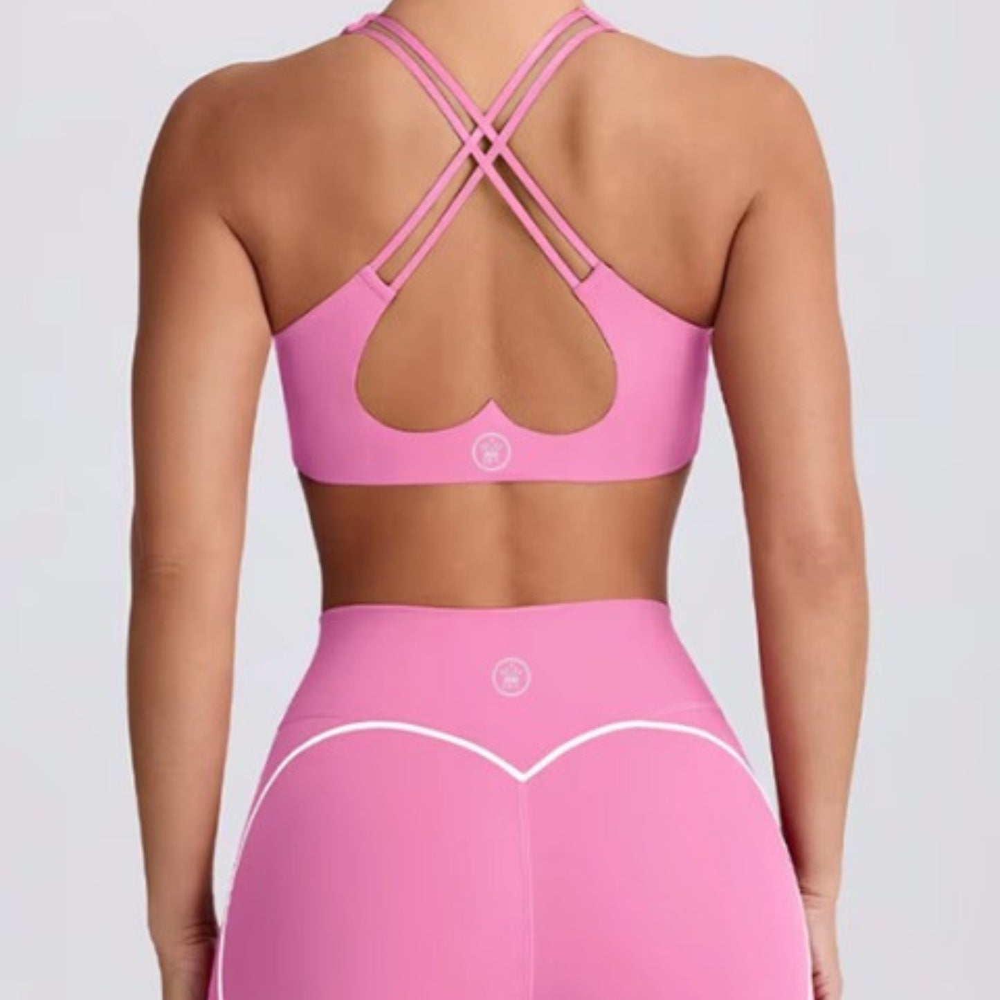 woman wearing DEW™ Women’s Sculpt Seamless Shorts - Pink Blush and DEW™ Strappy Heart Flex Sports Bra - Pink Blush, Pink sports bra and leggings set on a plain background