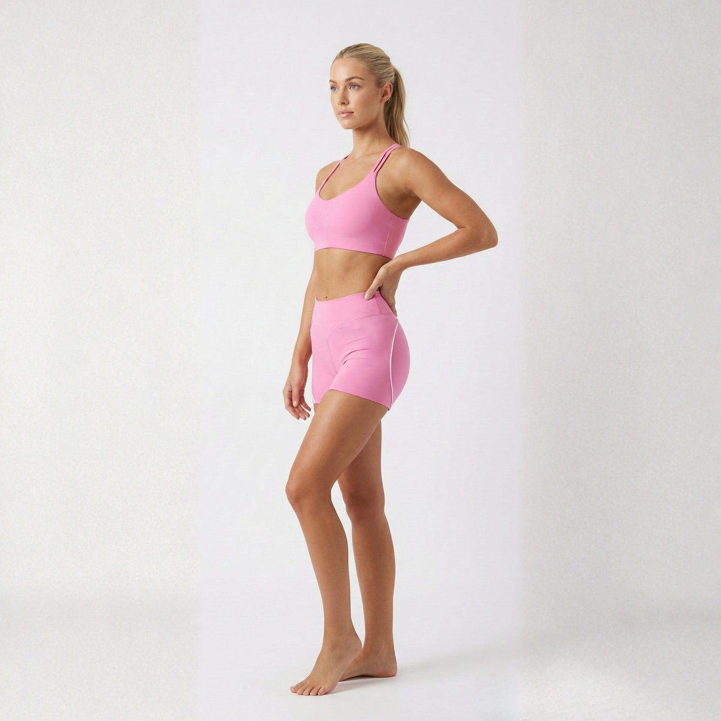 Woman wearing a DEW™ Women’s Sculpt Seamless Shorts - Pink Blush and DEW™ Strappy Heart Flex Sports Bra - Pink Blush, pink sports bra and shorts on a white background