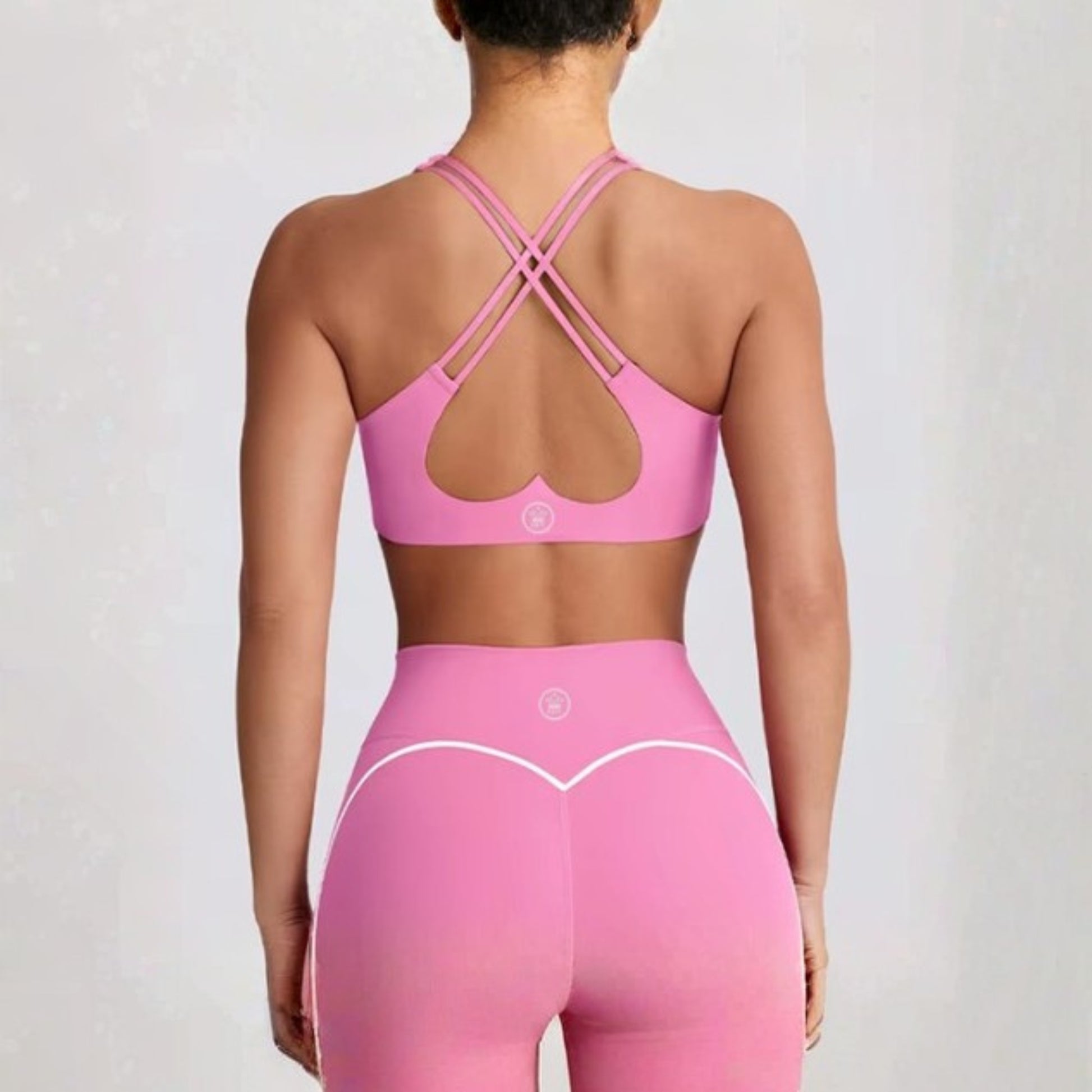 Person wearing a DEW™ Women’s Sculpt Seamless Shorts - Pink Blush and DEW™ Strappy Heart Flex Sports Bra - Pink Blush  pink sports bra and leggings set on a plain background