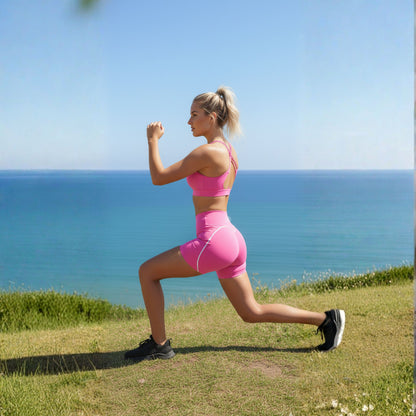 Woman in DEW™ Strappy Heart Flex Sports Bra - Pink Blush , pink athletic wear exercising outdoors with ocean in the background