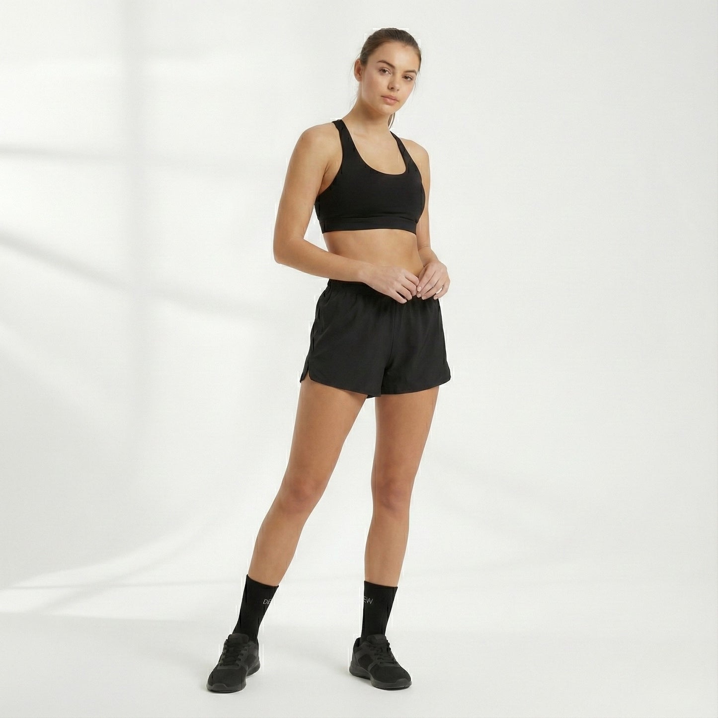 Woman wearing a black sports bra and shorts and Dew 100% Bamboo socks on a white background