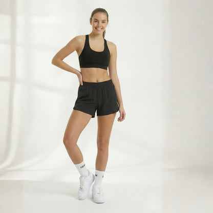 Woman wearing Dew 100% Bamboo socks a black sports bra and shorts set with white sneakers on a white background