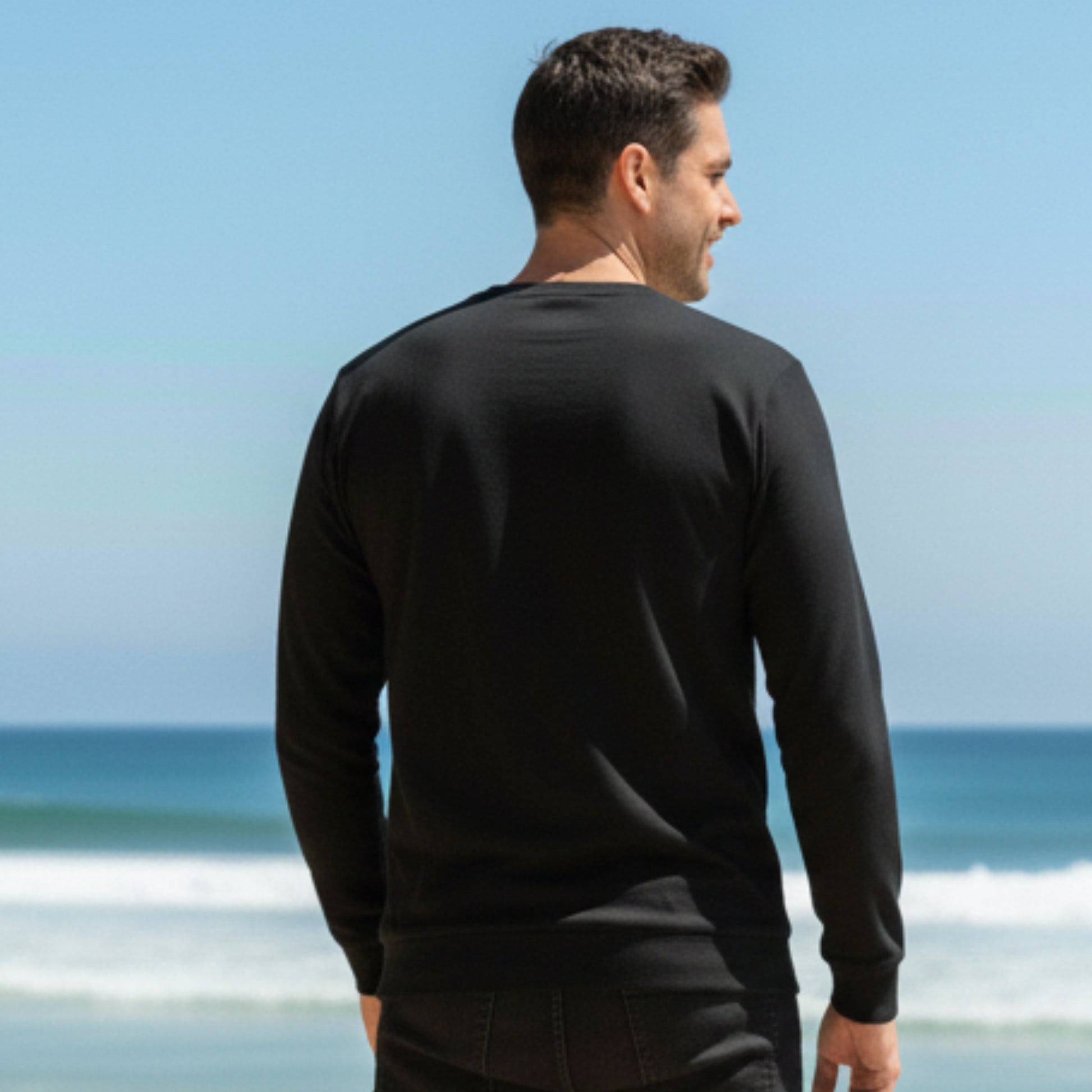 Man wearing a  Dew 100% Cotton black long-sleeve shirt standing on a beach with ocean view