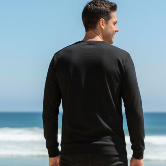 Man wearing a  Dew 100% Cotton black long-sleeve shirt standing on a beach with ocean view