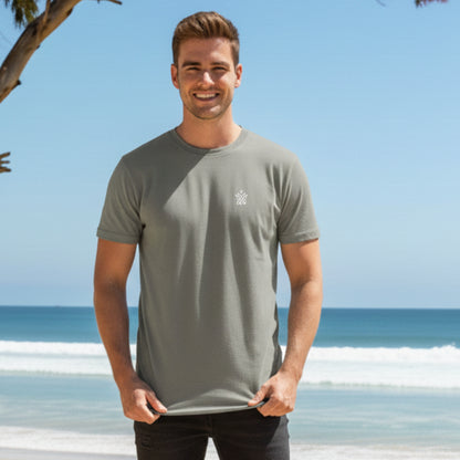 Man wearing a Dew 100% Cotton Rock Ash gray t-shirt with a logo on a beach