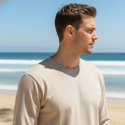 Man standing on a beach wearing a Dew 100% cotton beige long-sleeve shirt with ocean and sky in the background