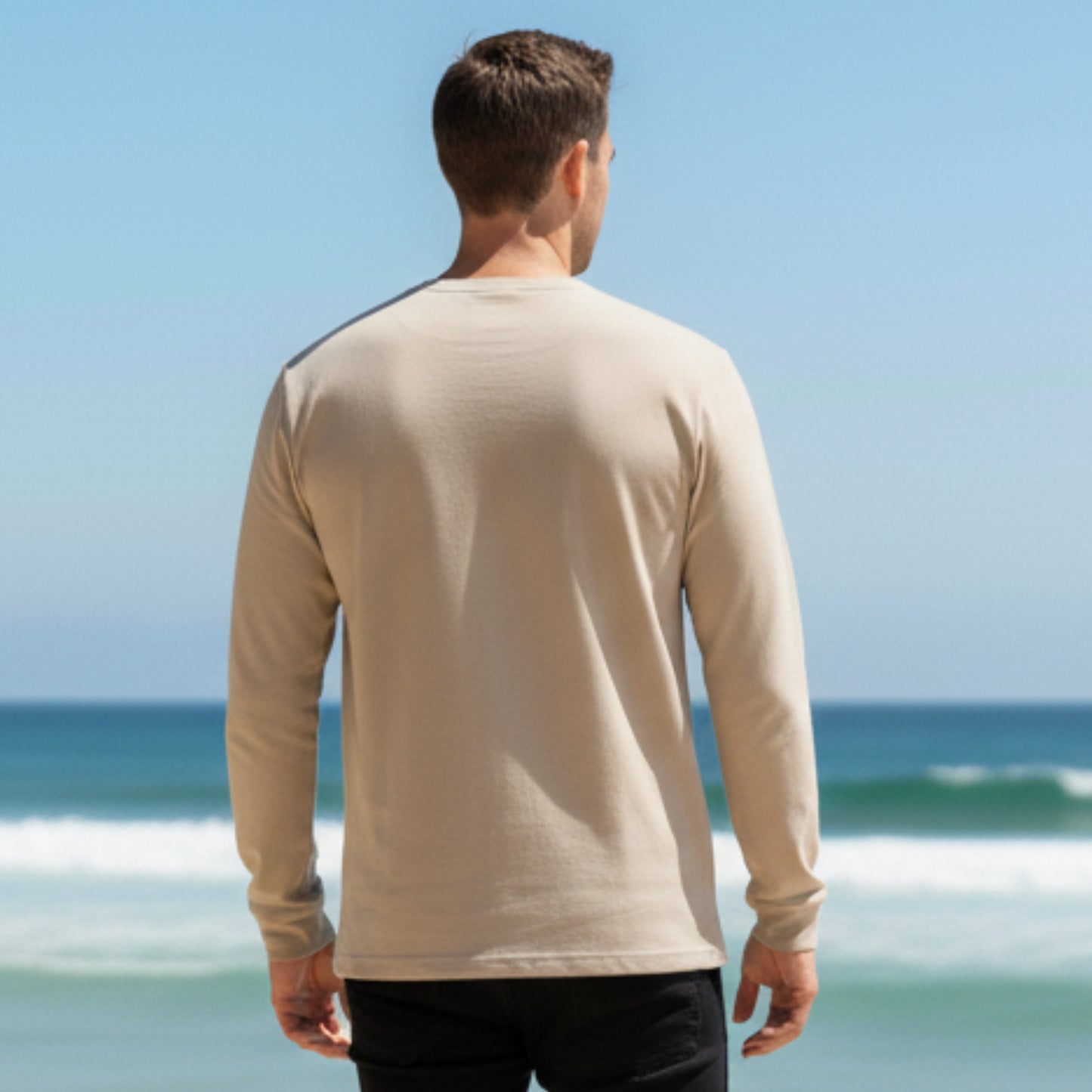 Man wearing a Dew 100% cotton beige long-sleeve shirt standing on a beach with ocean view