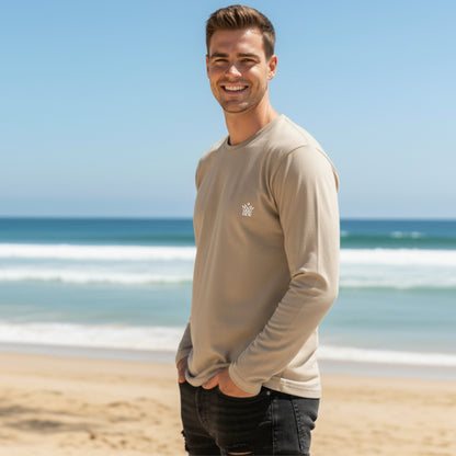 Man wearing a Dew 100% cotton caramel long-sleeve shirt on a beach with ocean in the background