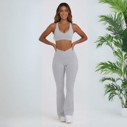 Woman wearing a gray Dew Flow fit flares athletic outfit standing next to a plant on a light background