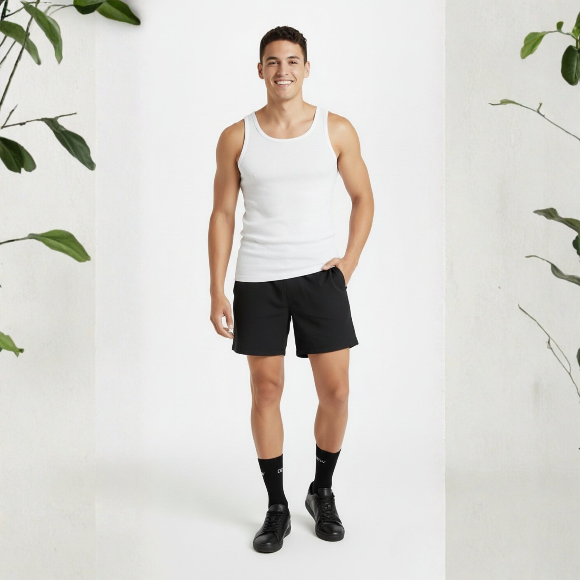 Man wearing a white tank top and black shorts on a white background with green plants.