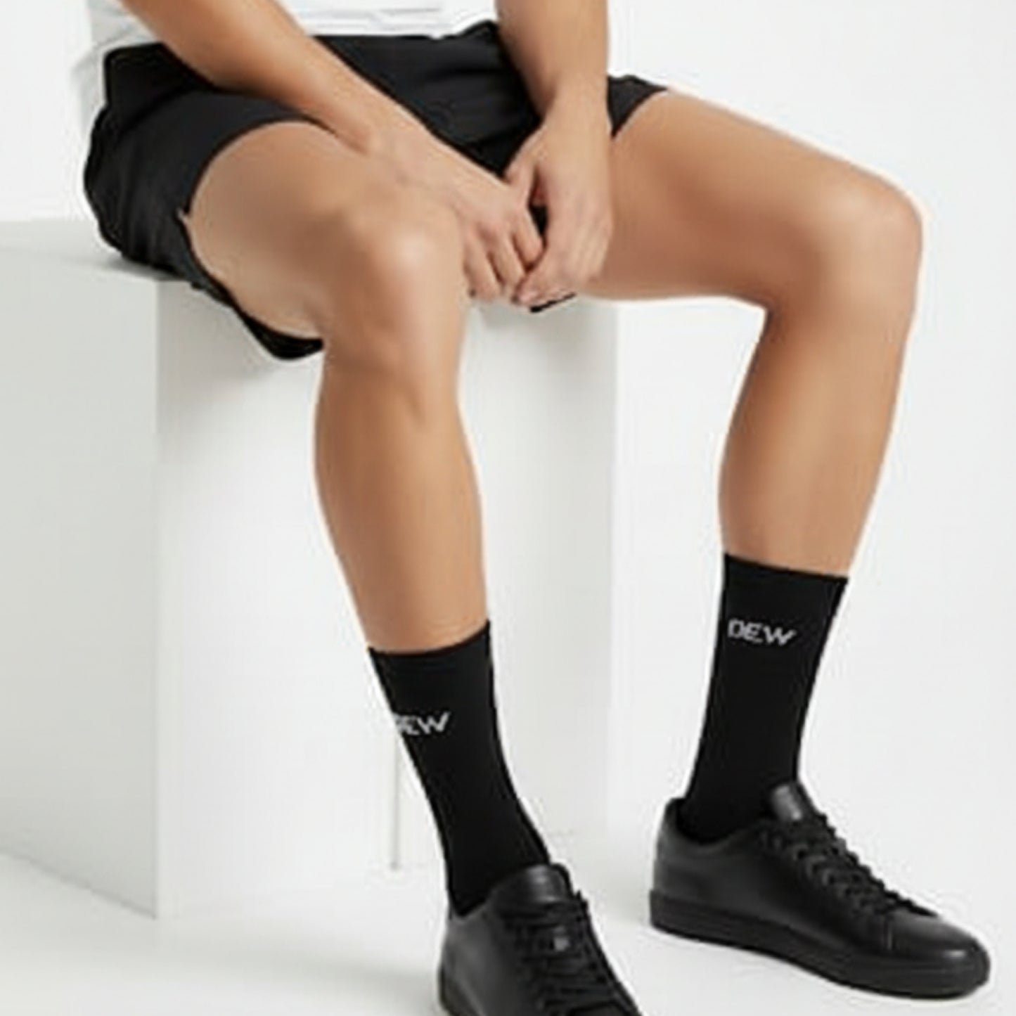 Person wearing black socks with 'DEW' branding sitting on a white surface.