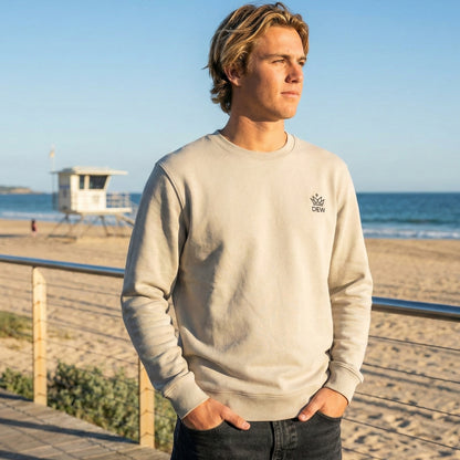Man wearing a Dew cream crewneck jumper with a logo on a beach