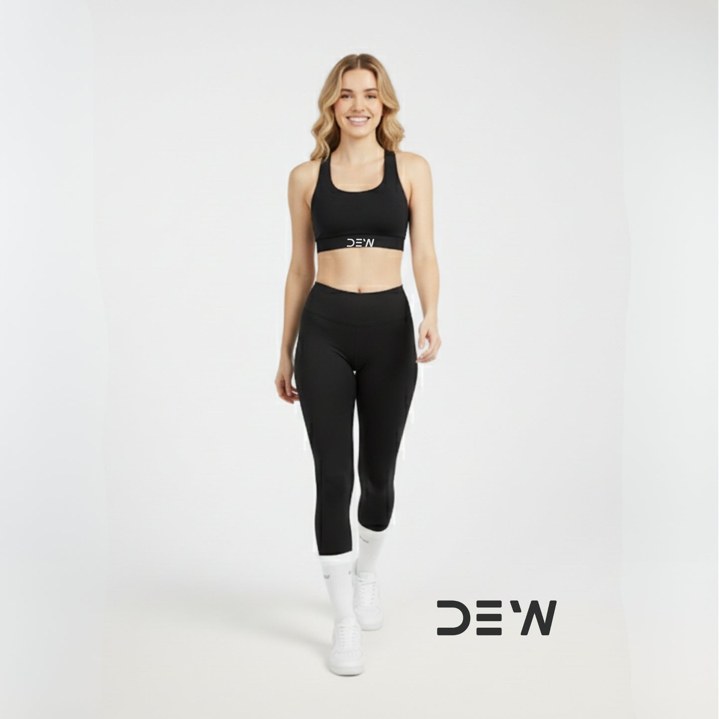 Woman wearing a black sports bra, leggings  and white Dew socks with 'DEW' branding on a white background