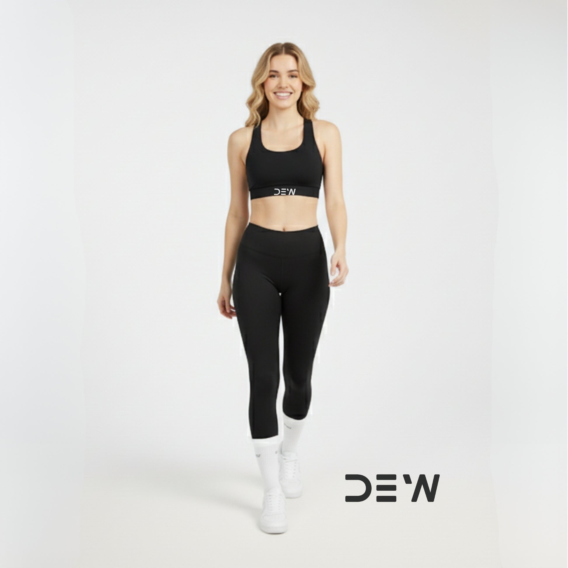 Woman wearing a black sports bra, leggings  and white Dew socks with 'DEW' branding on a white background