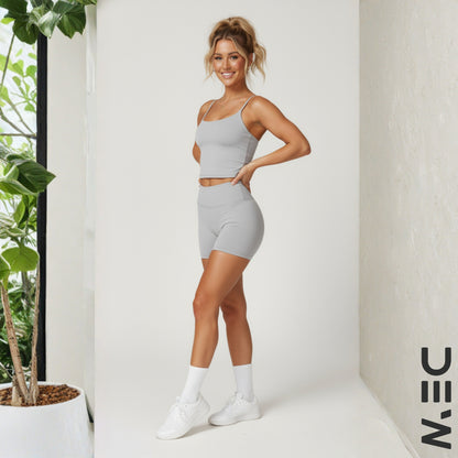 Woman in gray DEW luxe cami top and shorts standing indoors with a plant in the background