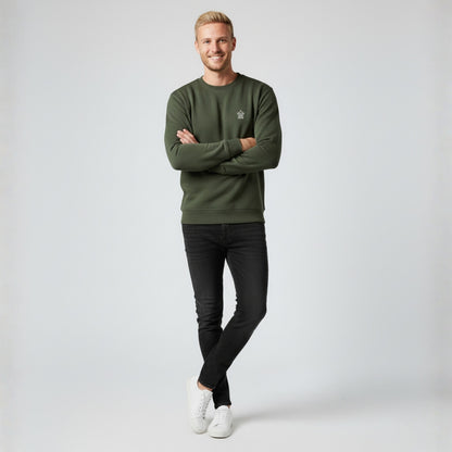 Man wearing a Dew olive green crewneck jumper and black pants standing against a white background