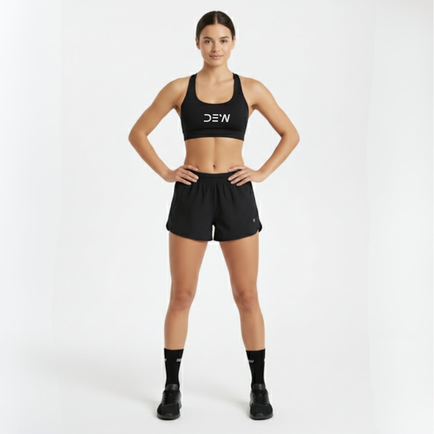 Woman wearing a black sports bra and shorts with 'DEW' branding on a white background