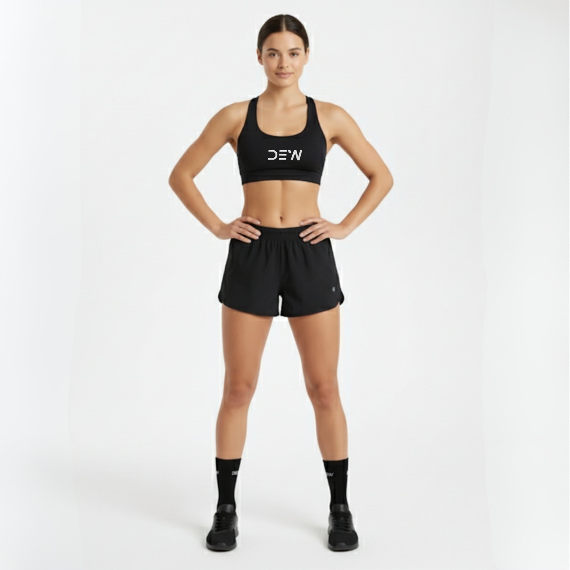 Woman wearing a black sports bra and shorts with 'DEW' branding on a white background