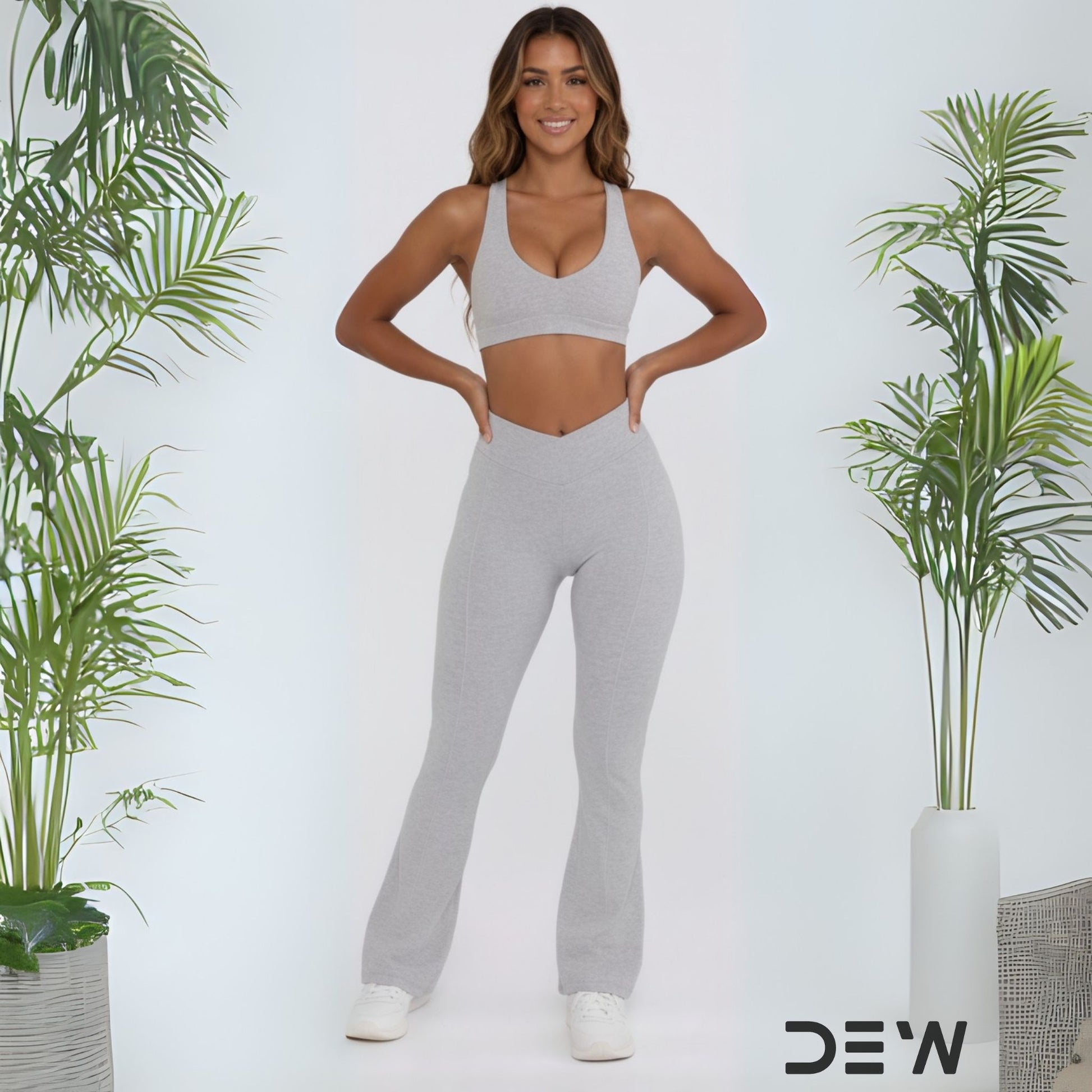 Woman wearing gray seamless flare leggings and matching sports bra. Full length shot highlighting flare fit and DEW branding.