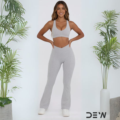 Woman wearing gray seamless flare leggings and matching sports bra. Full length shot highlighting flare fit and DEW branding.