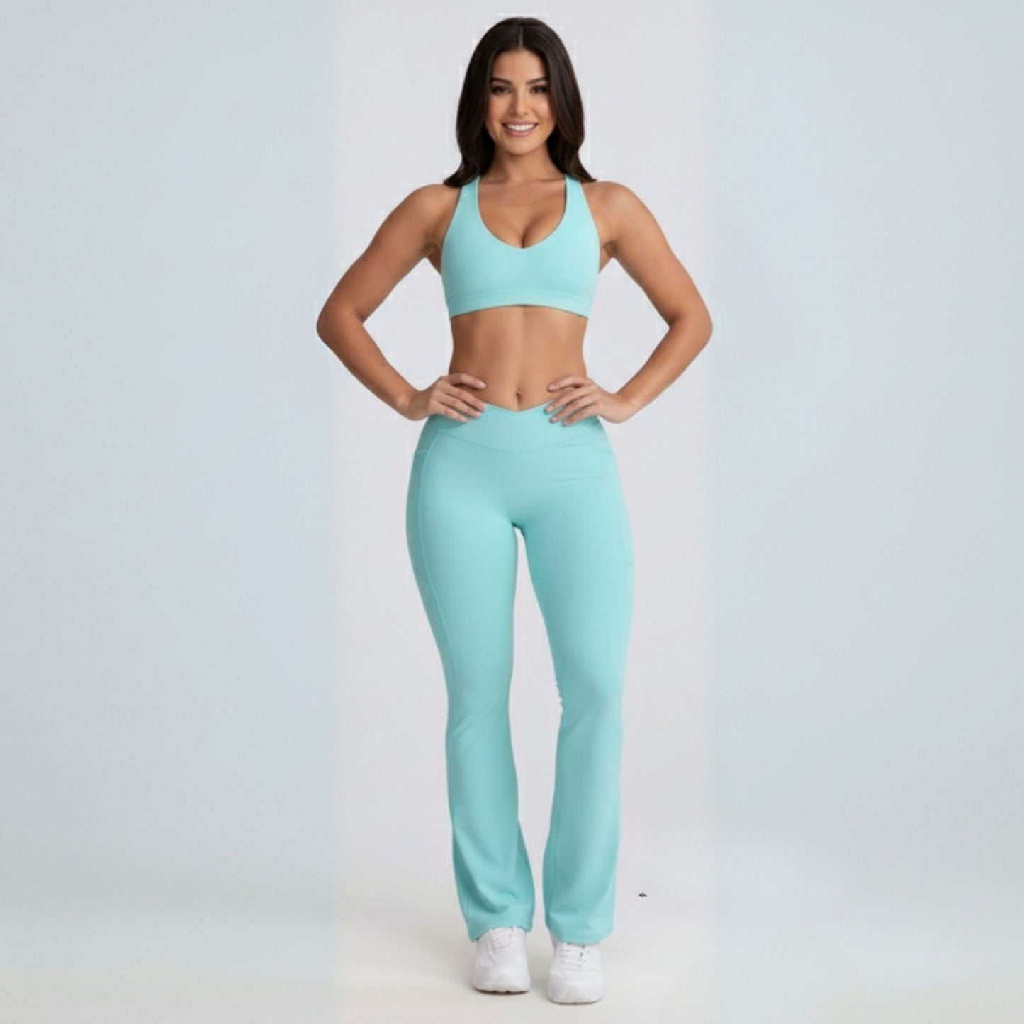 Woman wearing a matching mint Dew Flow fit flares sports bra and leggings set on a light gray background