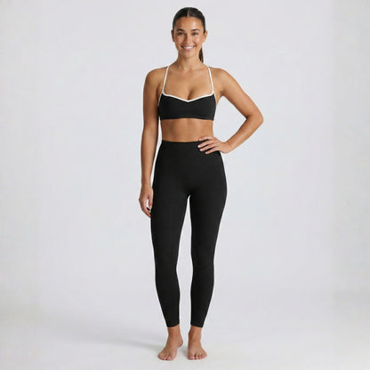 Woman wearing a black DEW Elevate sports bra and leggings on a white background