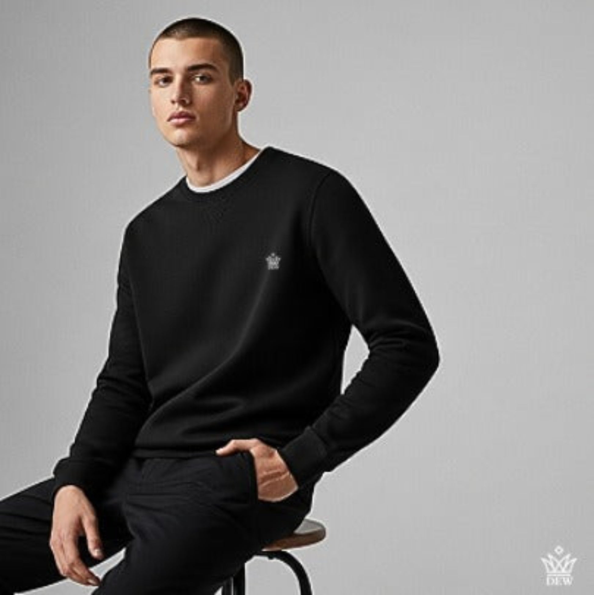Man wearing a  black Dew Classic Jumper with a logo on a gray background