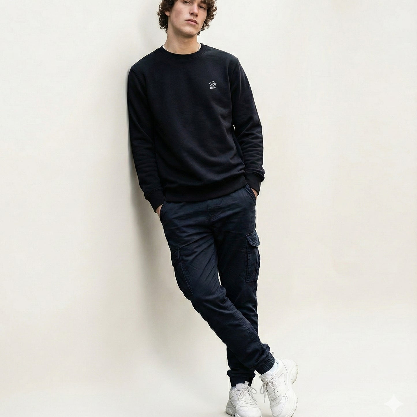 Person wearing a  black Dew Classic Jumper and navy cargo pants against a white wall