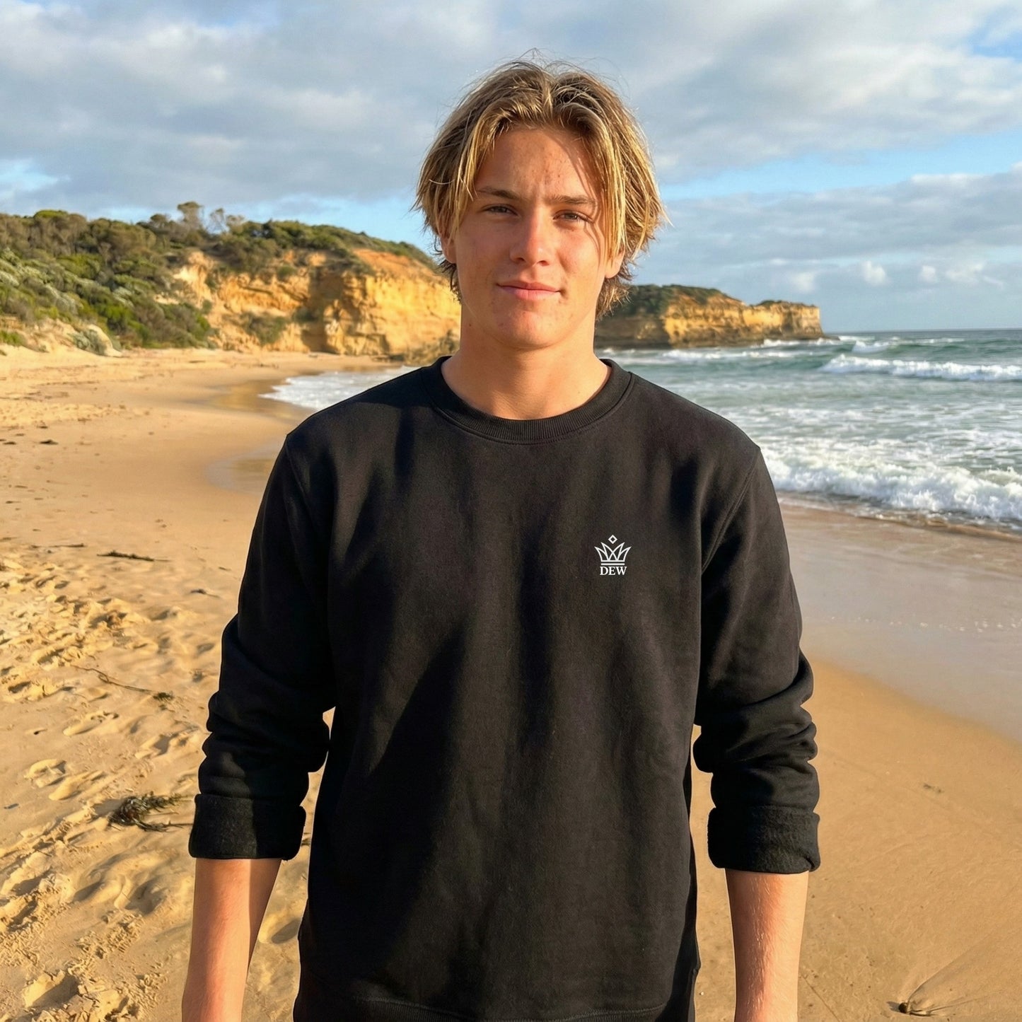 Person wearing a  black Dew Classic Jumper with a logo on a beach