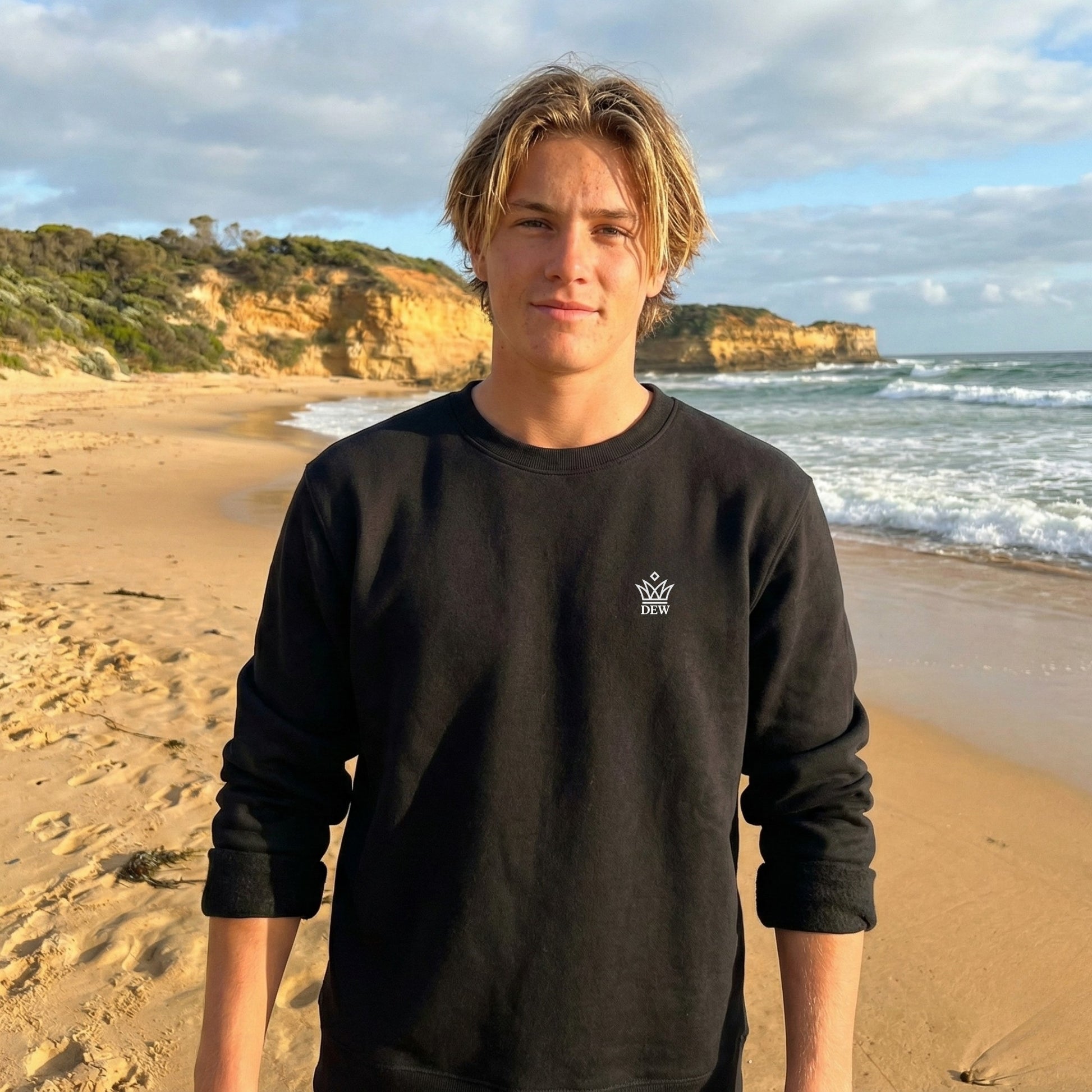 Person wearing a  black Dew Classic Jumper with a logo on a beach