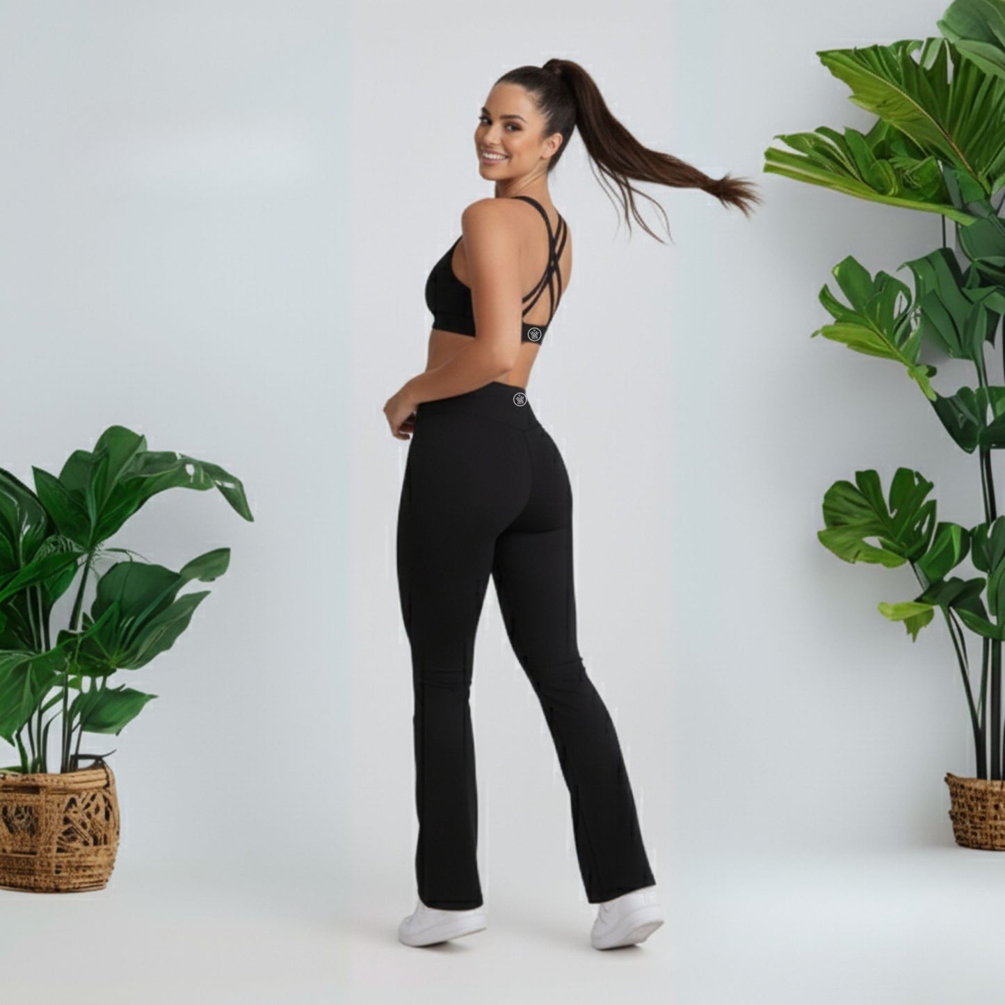 Woman wearing black  black dew flow fit flares  athletic pants and sports bra standing in a minimalistic setting with plants.