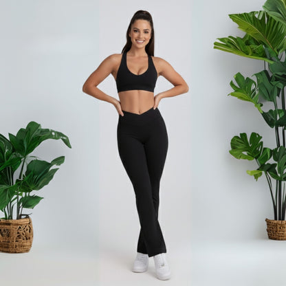 Woman in black  black dew flow fit flares  athletic wear standing between two potted plants on a white background