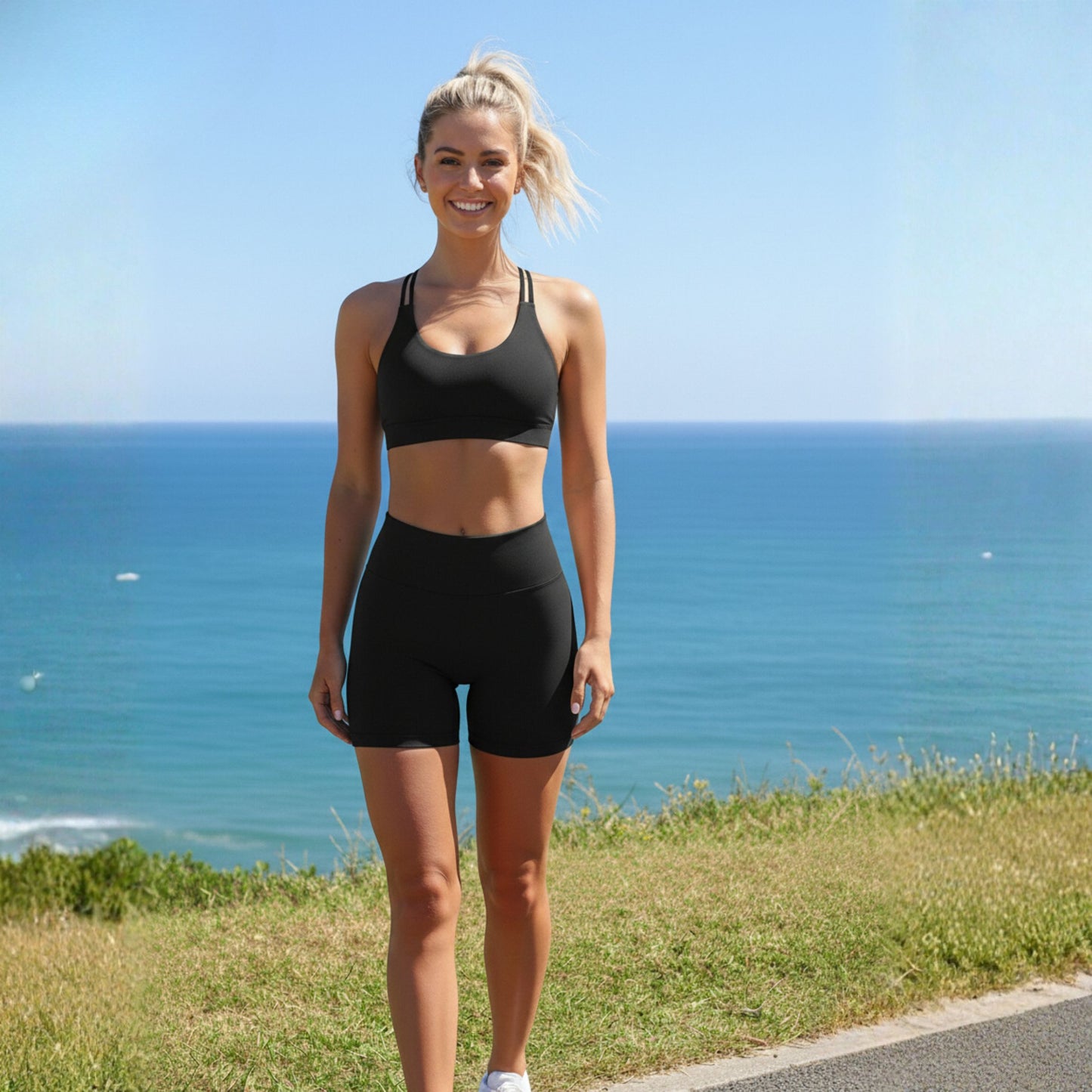Woman in black dew heart flex bra standing on a grassy area with ocean view