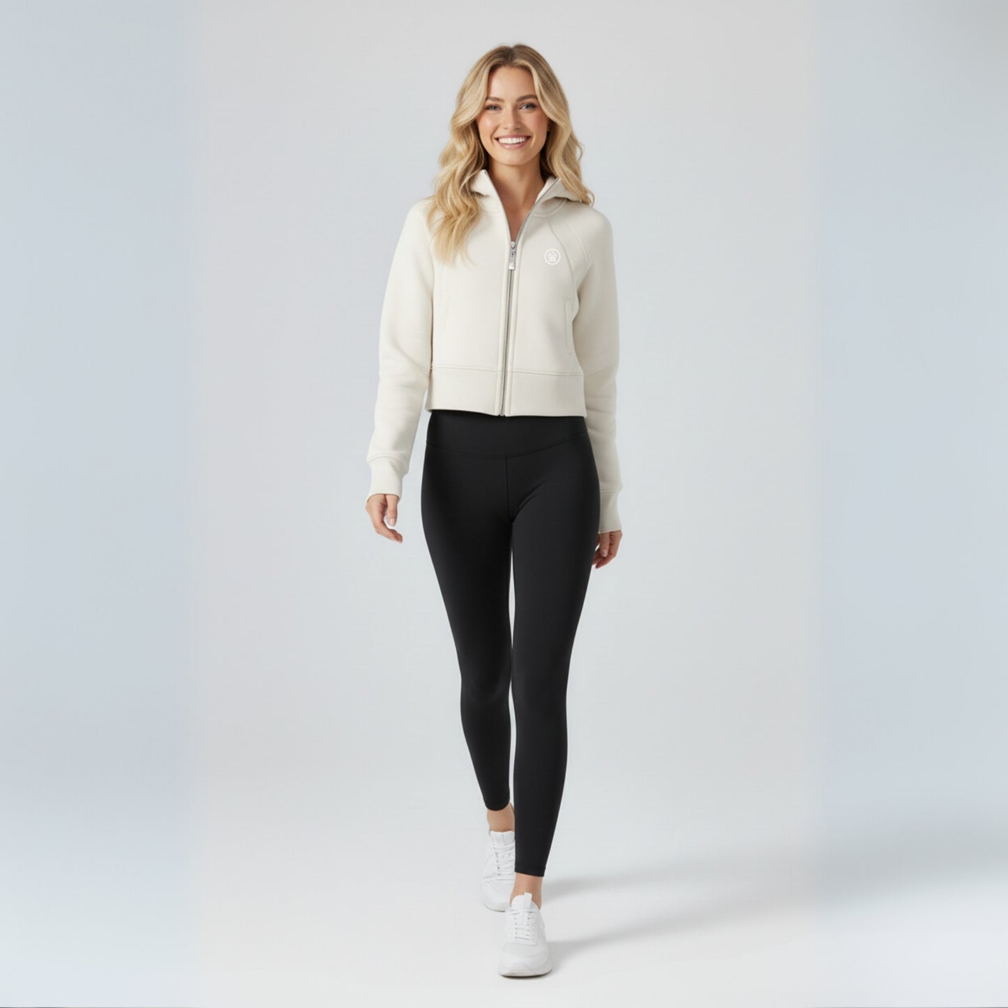 Woman wearing a cream zip-up jacket and black dew leggings on a white background