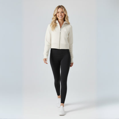 Woman wearing a cream zip-up jacket and black dew leggings on a white background